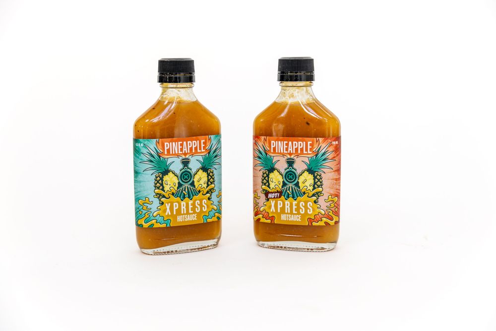 Two identical glass bottles of Trukulu hot sauce with orange liquid and turquoise labels displayed on white background.