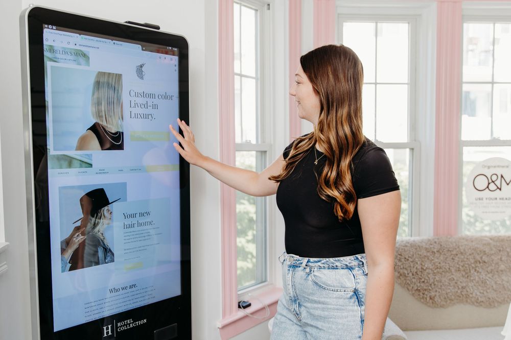 Someone interacts with a large vertical touchscreen display while wearing a black t-shirt and light denim jeans.