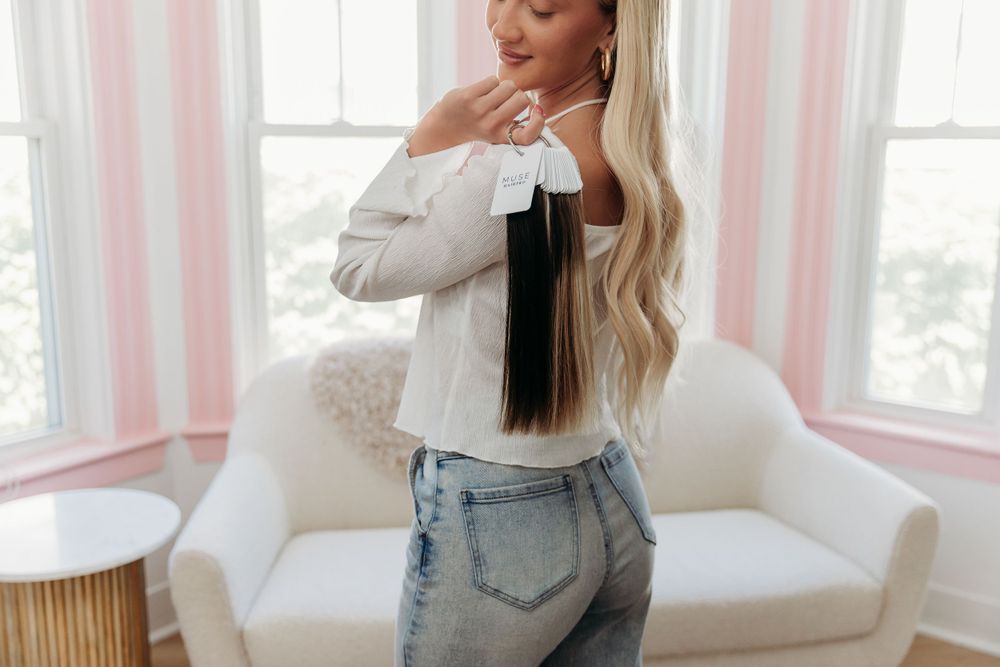 Long blonde hair cascading down a white off shoulder sweater paired with light wash denim jeans in a bright room setting.