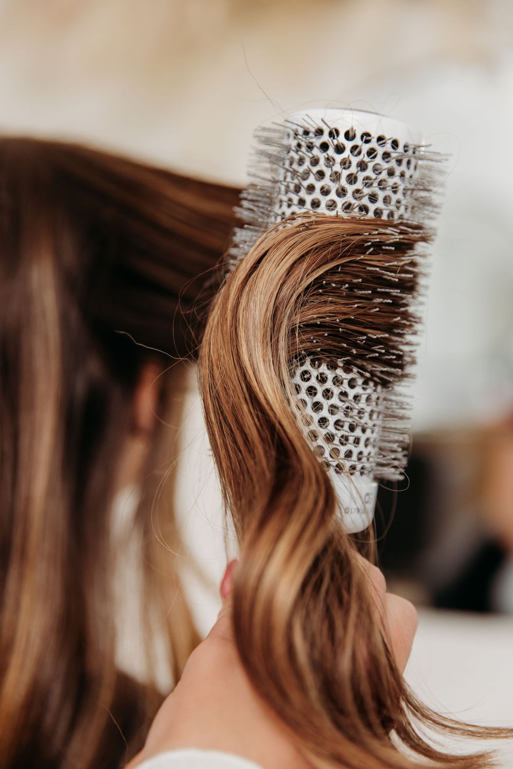Close-up view of a round brush wrapped with brown hair during a styling session at a salon.