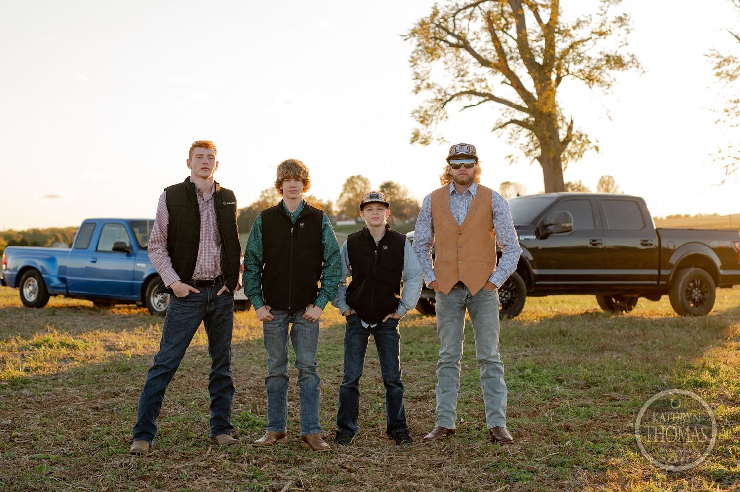 Four people posing outdoors with pickup trucks parked behind them during sunset.