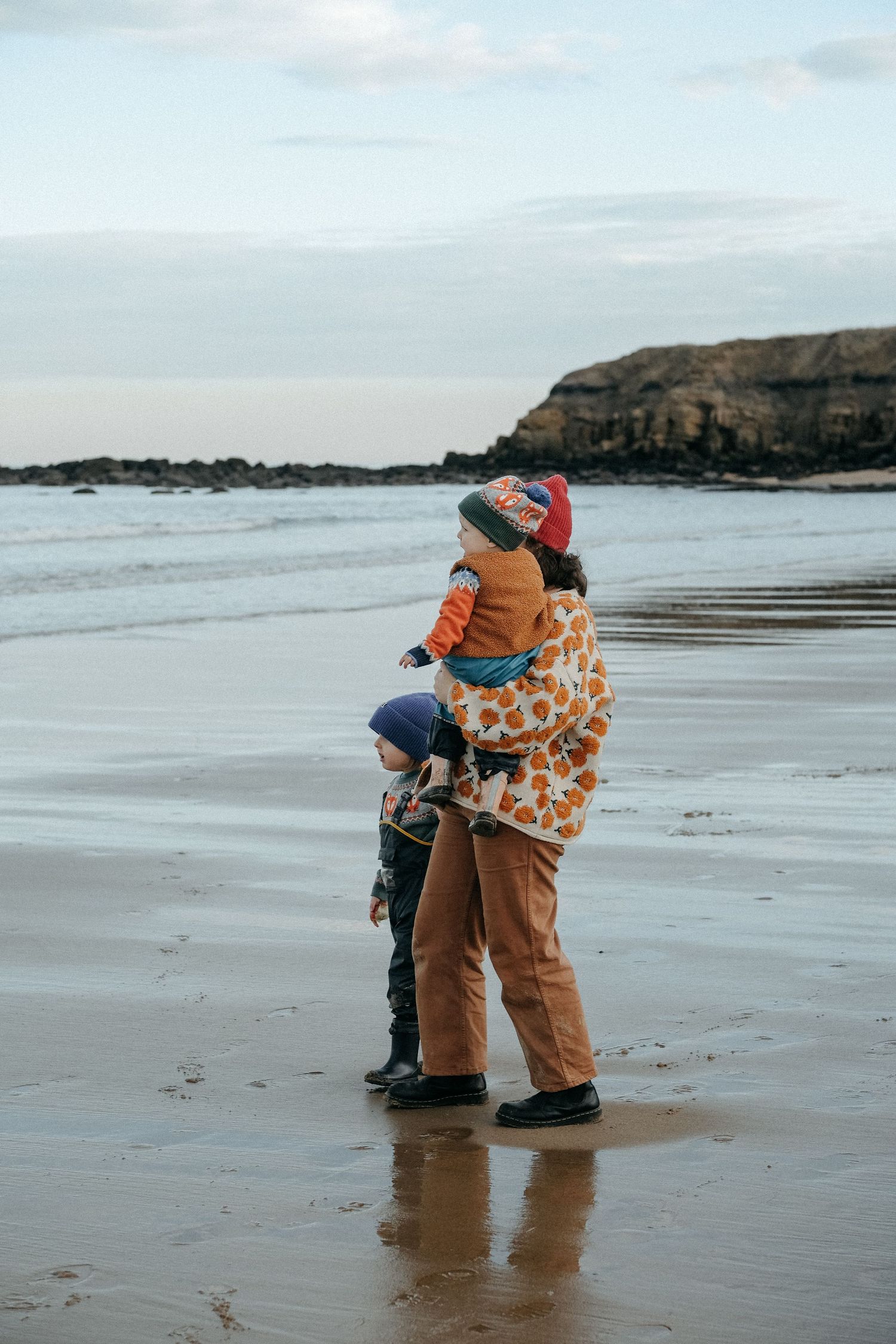 A tender embrace between parent and child on a cloudy beach with cliffs in the background.