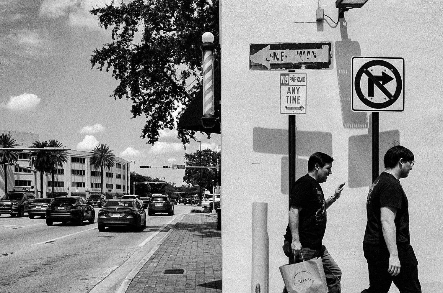 A black and white urban street scene showing parked cars and street signs.