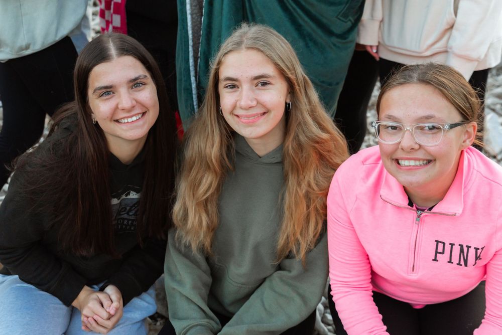 Three friends sitting together and smiling in casual winter clothing.