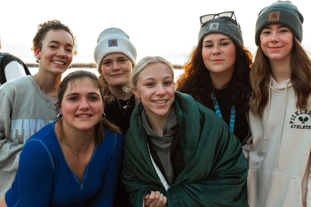 Group of friends huddled together outdoors wearing winter clothing and beanies.