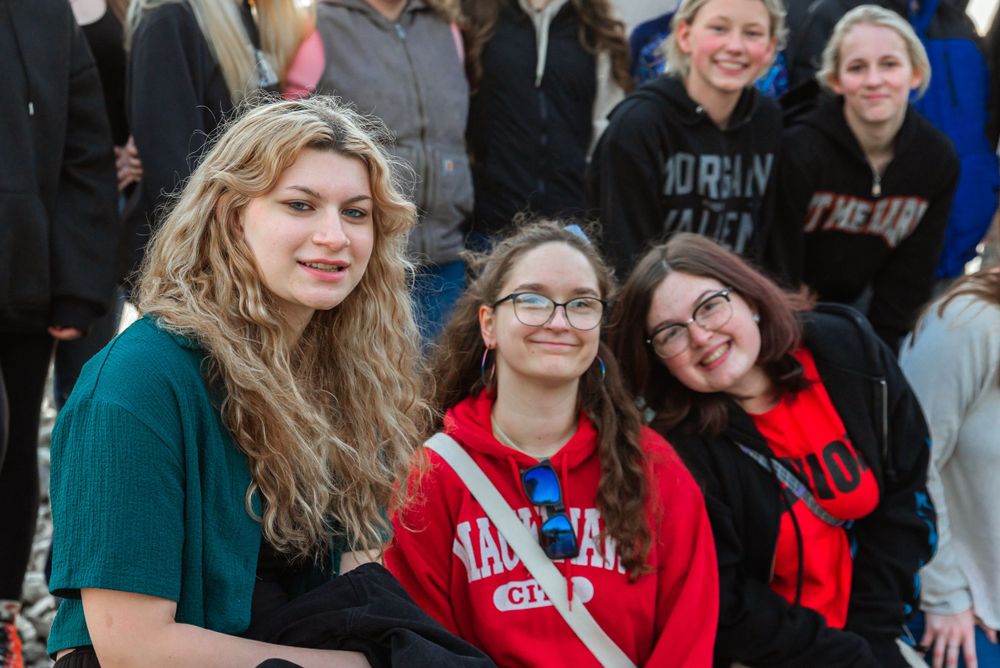 Three friends sitting together outdoors wearing casual winter clothing.