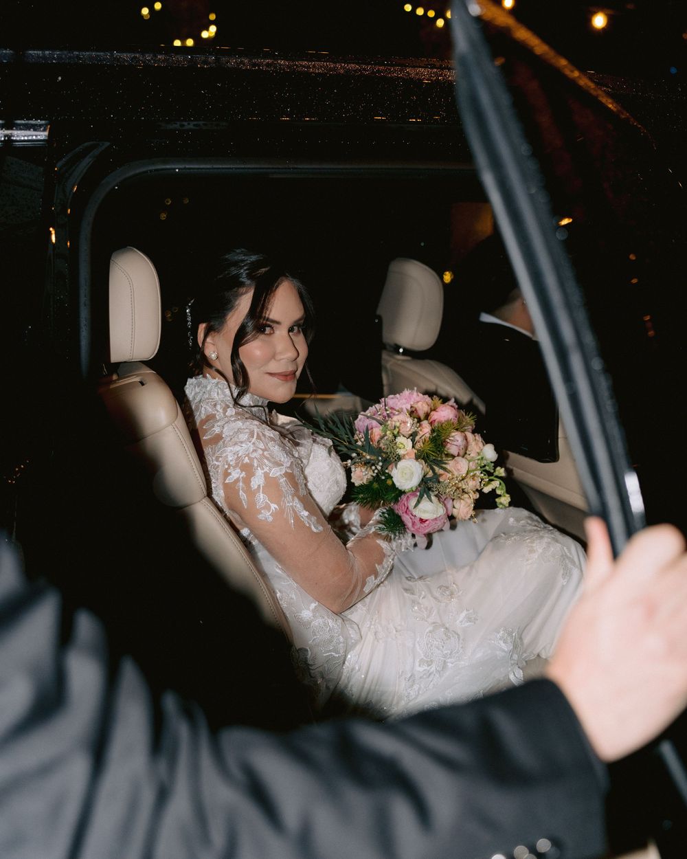 Bride sitting in the car after the wedding ceremony, holding her bouquet during a romantic nighttime exit