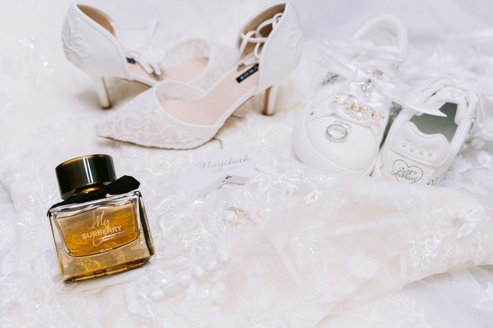 Flat-lay of bridal wedding details including lace heels, perfume bottle and accessories