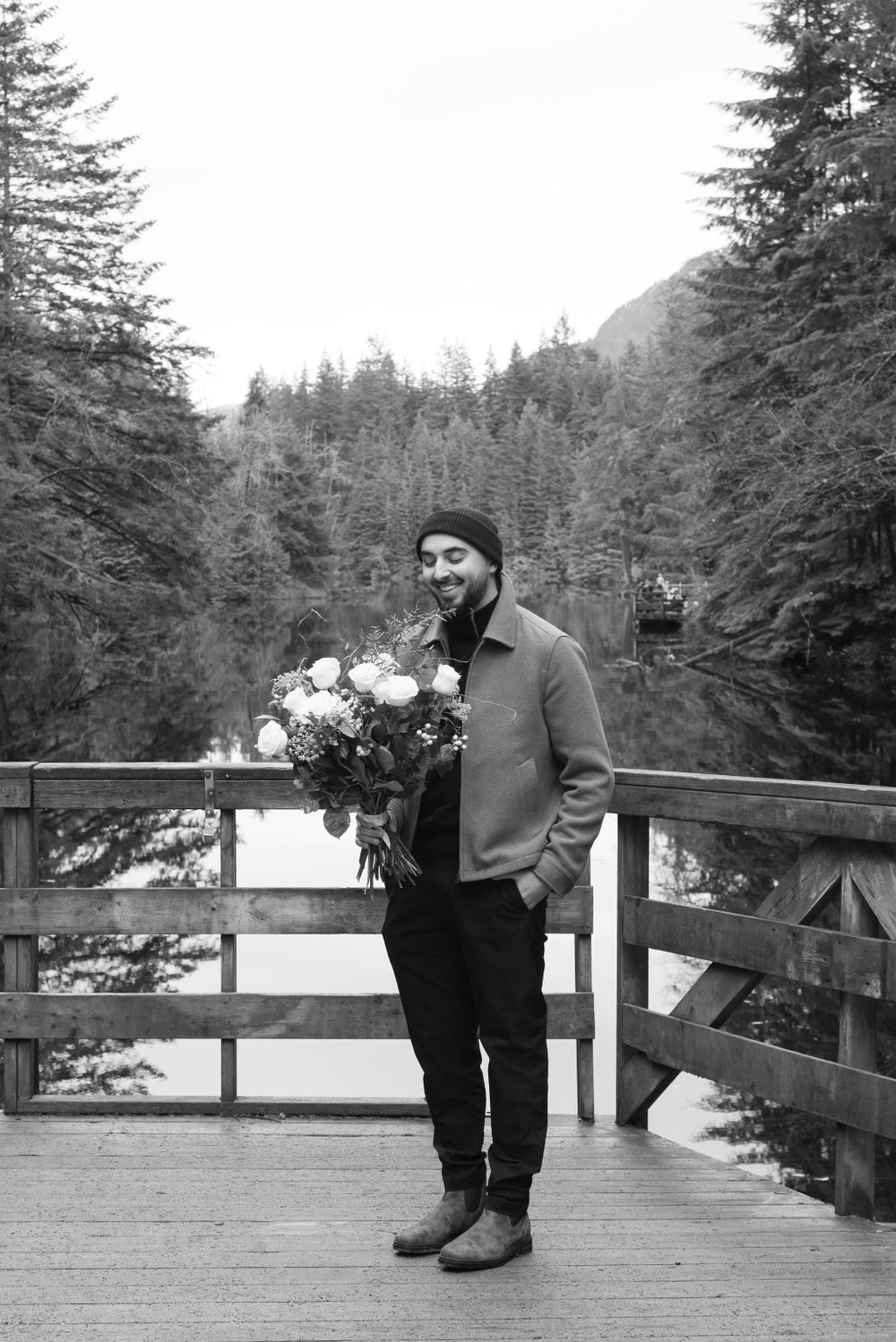 Black and white photo showing a romantic scene on a wooden deck with evergreen trees in background.