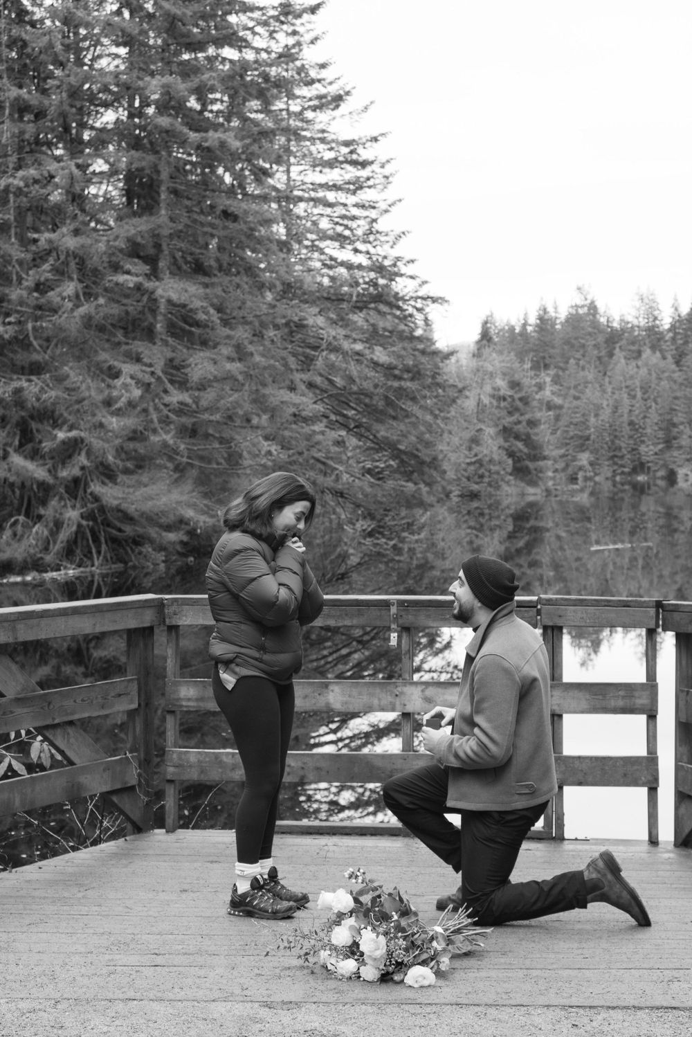 A couple shares a special moment on a wooden deck overlooking a snowy winter forest landscape.