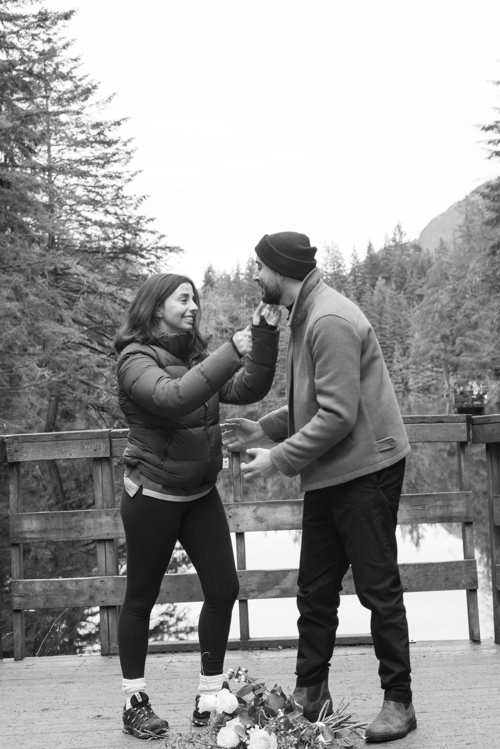 A couple shares an intimate moment on a wooden observation deck surrounded by snow-capped evergreens.