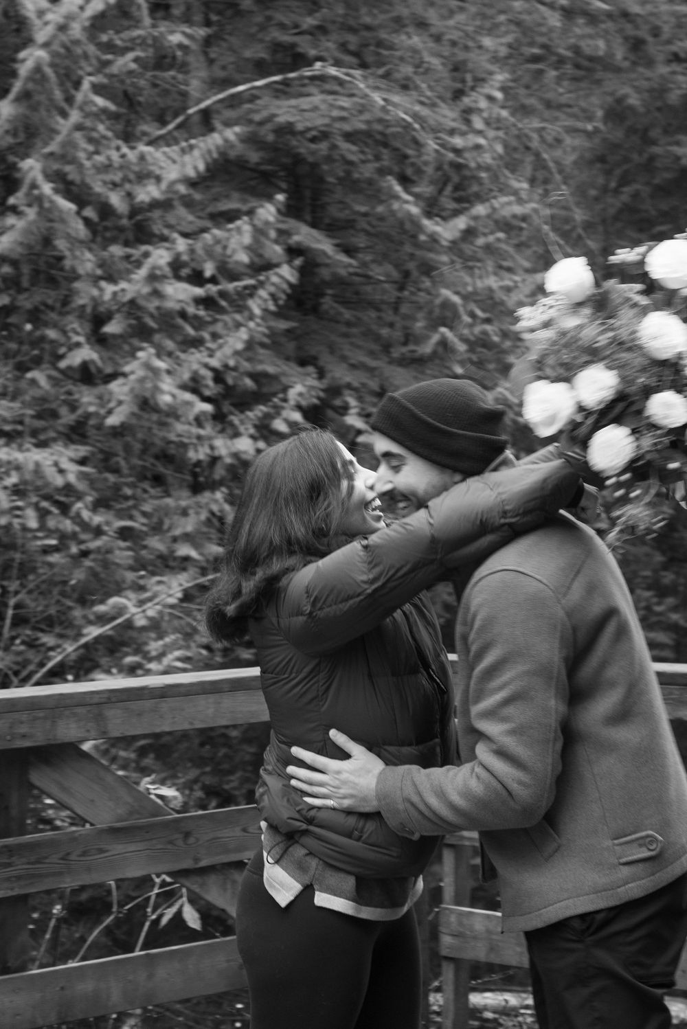 A romantic black and white scene unfolds on a wooden deck with forest and mountain views.
