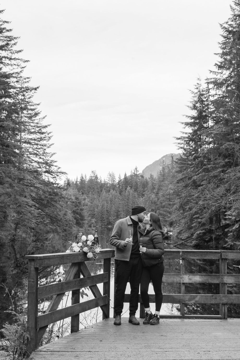 Wide view of wooden observation deck with mountains and evergreen forest in background.