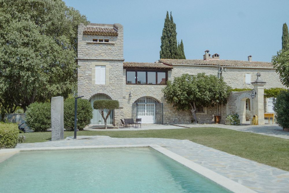 Stone building exterior with swimming pool and cypress trees in Mediterranean setting.