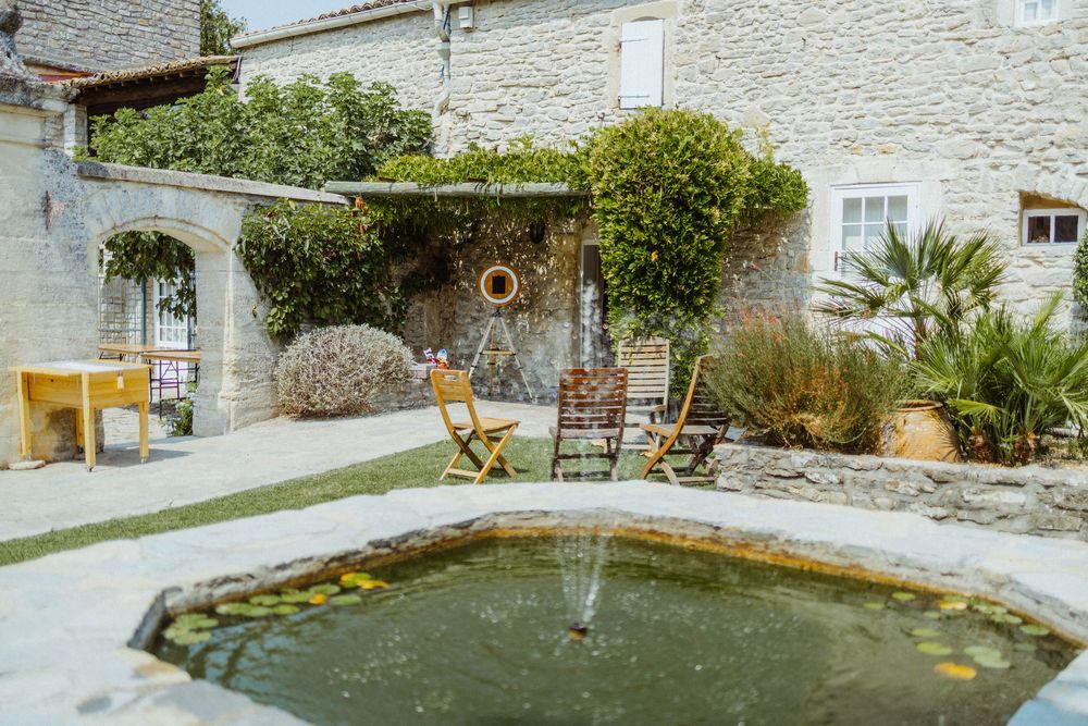 Stone building exterior with garden and water feature on a sunny day.