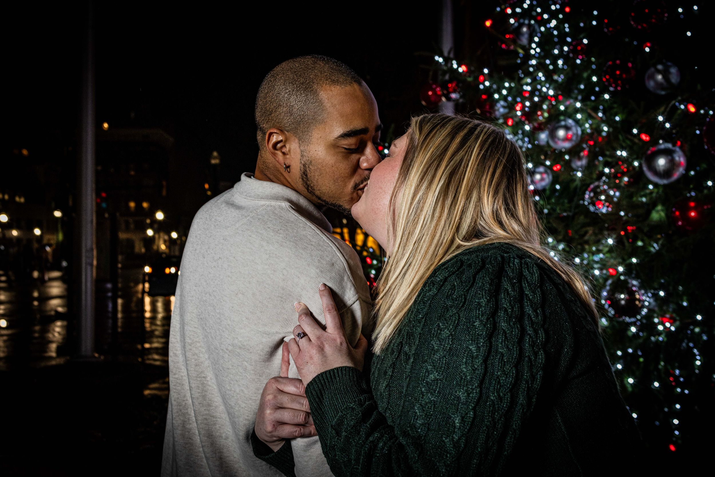 Engagement couple posing for shots after proposal in front of a Christmas tree on 2nd street in Harrisburg.