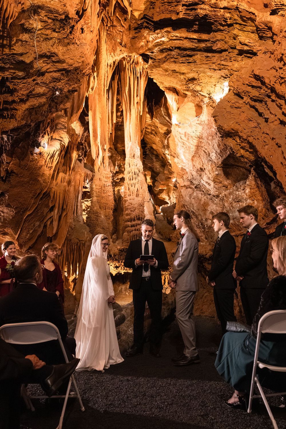 A bride and groom exchange vows in a stunning cave wedding ceremony surrounded by glowing stalactites and guests.