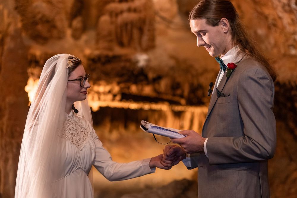 Couple exchanging vows in a cave wedding ceremony, bride in white gown and veil, groom in gray suit.
