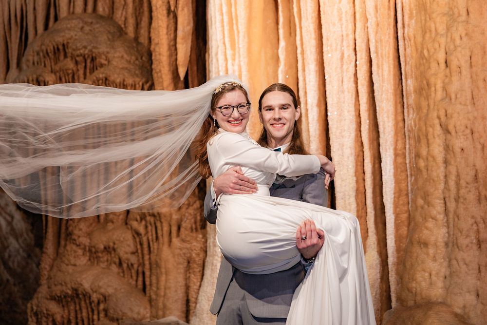 Bride and groom pose joyfully in a stunning cave wedding setting surrounded by stalactites.