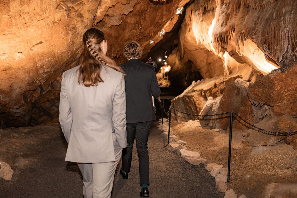Bride and groom walking through a stunning cave wedding venue with dramatic rock formations and ambient lighting.