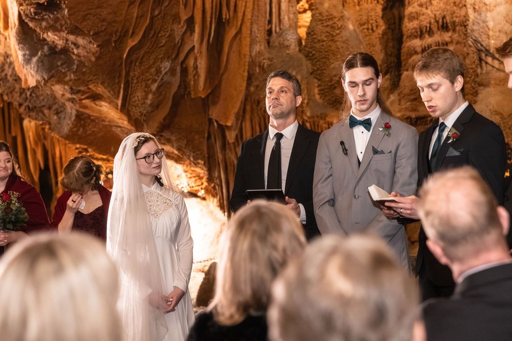 Wedding ceremony in a cave with bride, groom, and officiant standing before guests amid stunning rock formations.