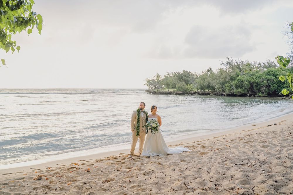 Bride and groom stand together on a tropical beach shoreline during their destination wedding ceremony.