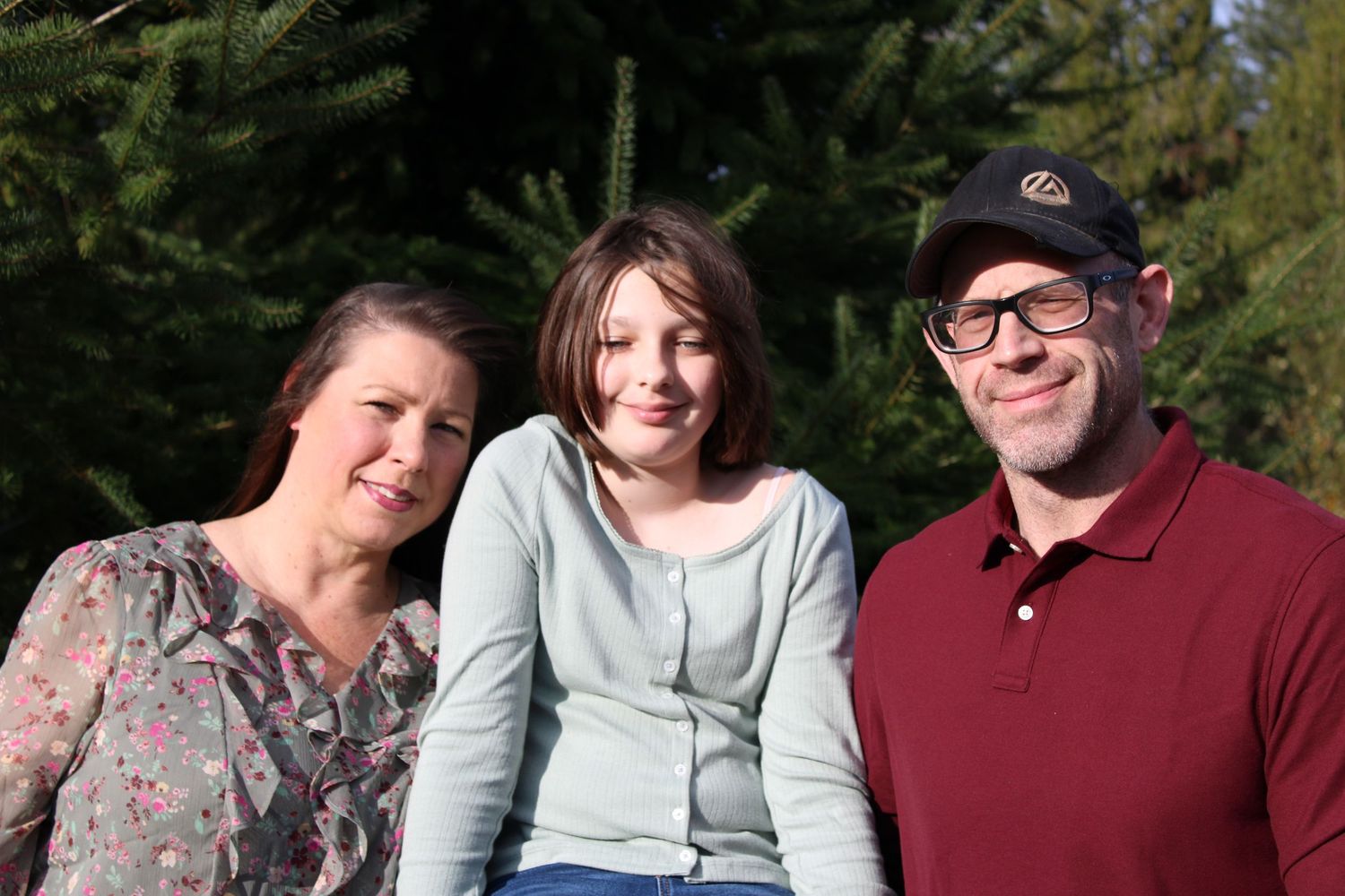 Family of three smiling together outdoors, natural portrait in forest setting
