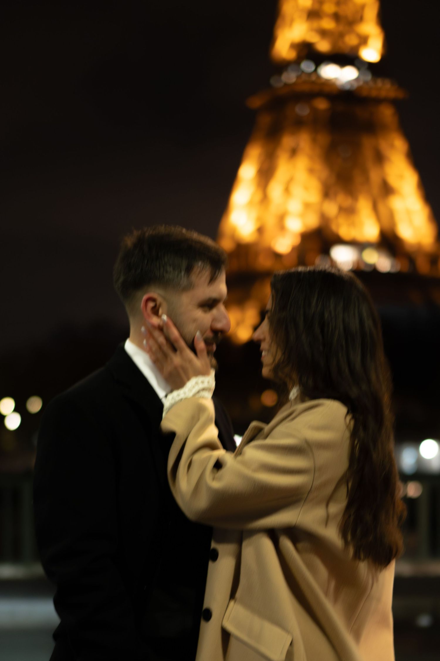 Romantic couple sharing a tender moment in front of the illuminated Eiffel Tower at night in Paris. Paris editorial eiffel tower photos.