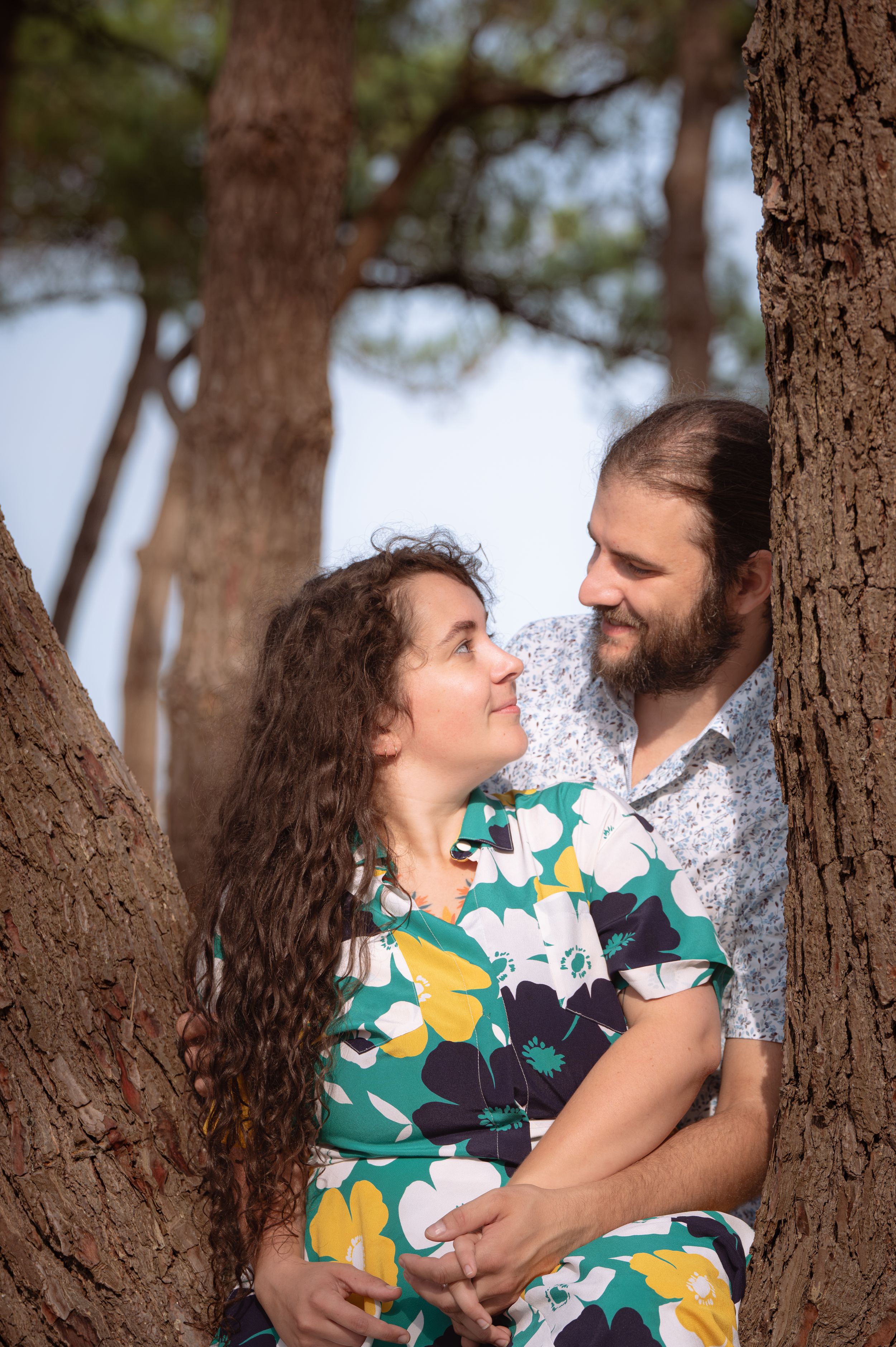 Un couple s'embrasse romantiquement entre des troncs d'arbres, se souriant dehors.