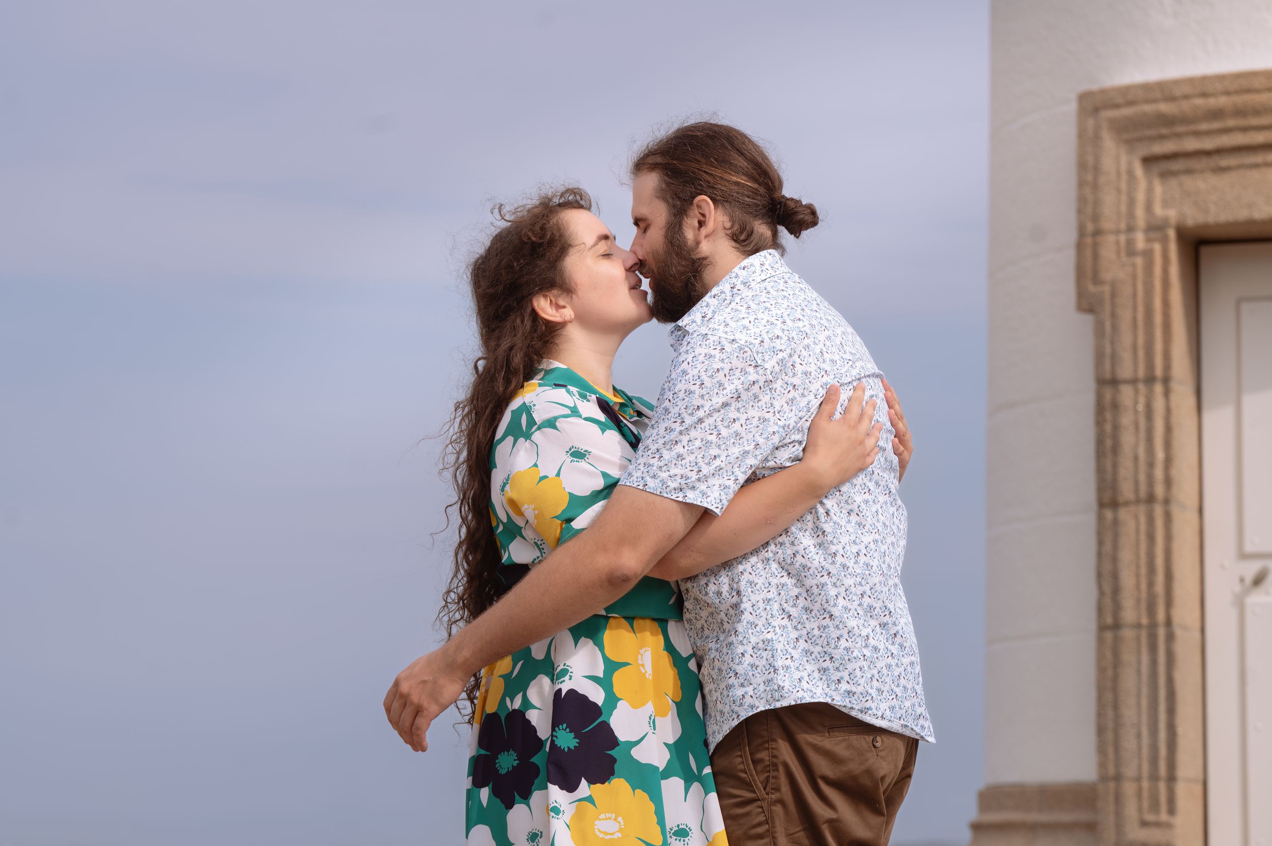 Un couple s'embrasse dehors, une femme en robe fleurie, un homme en chemise à motifs.