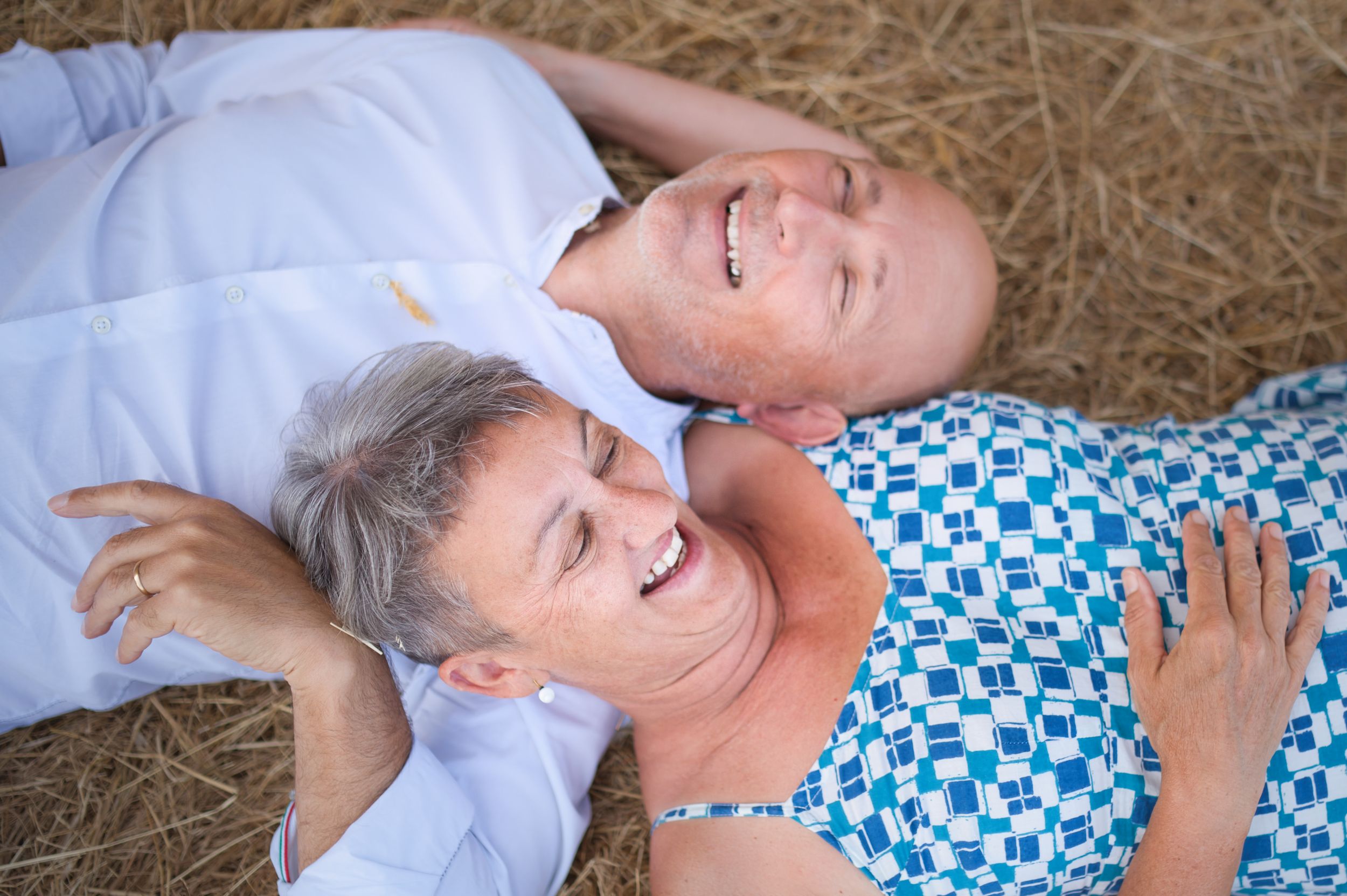 Un couple d'âge mûr rayonnant de joie, riant ensemble, allongés sur des bottes de foin dorées en plein air.