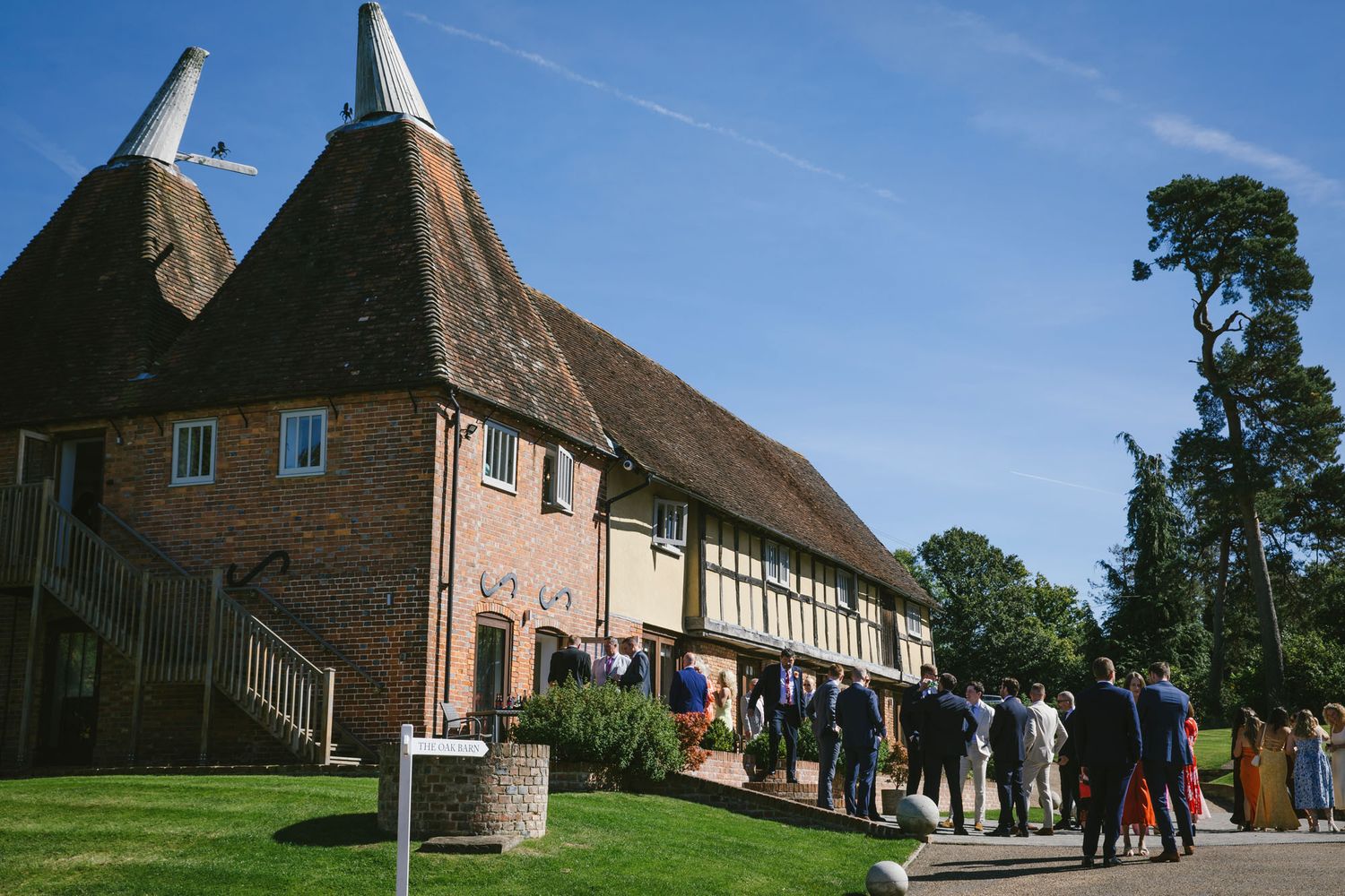 Guests gather outside a traditional Kent oast house venue on a sunny day for a wedding reception.