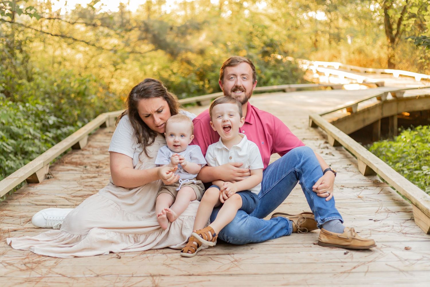 Fall family portrait with autumn leaves covering the ground in a wooded setting.