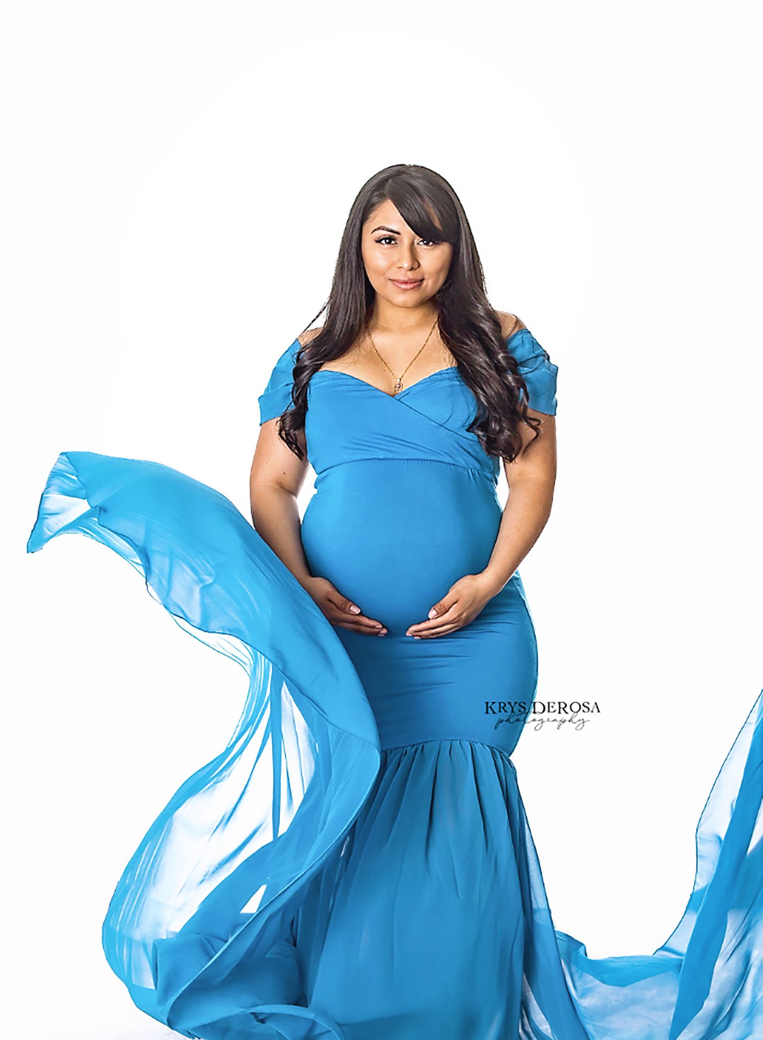 Pregnant woman in blue gown with husband and daughter in golden field at sunset maternity photography session.