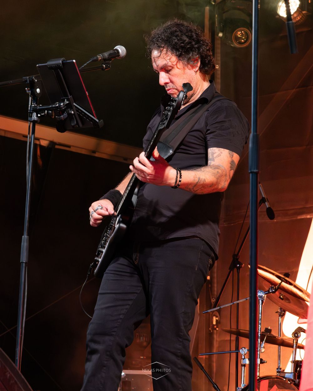 Male guitarist in black outfit playing electric guitar on stage near microphone stand.