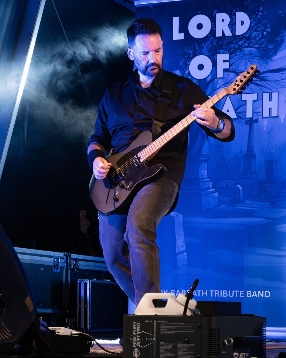 Guitarist performs on stage at Lord of Death Black Sabbath tribute band concert under blue stage lighting.