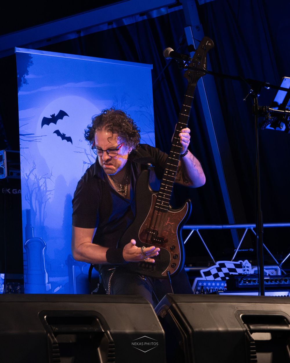 Bass guitarist passionately plays on stage at a Halloween-themed rock concert under dramatic blue lighting.