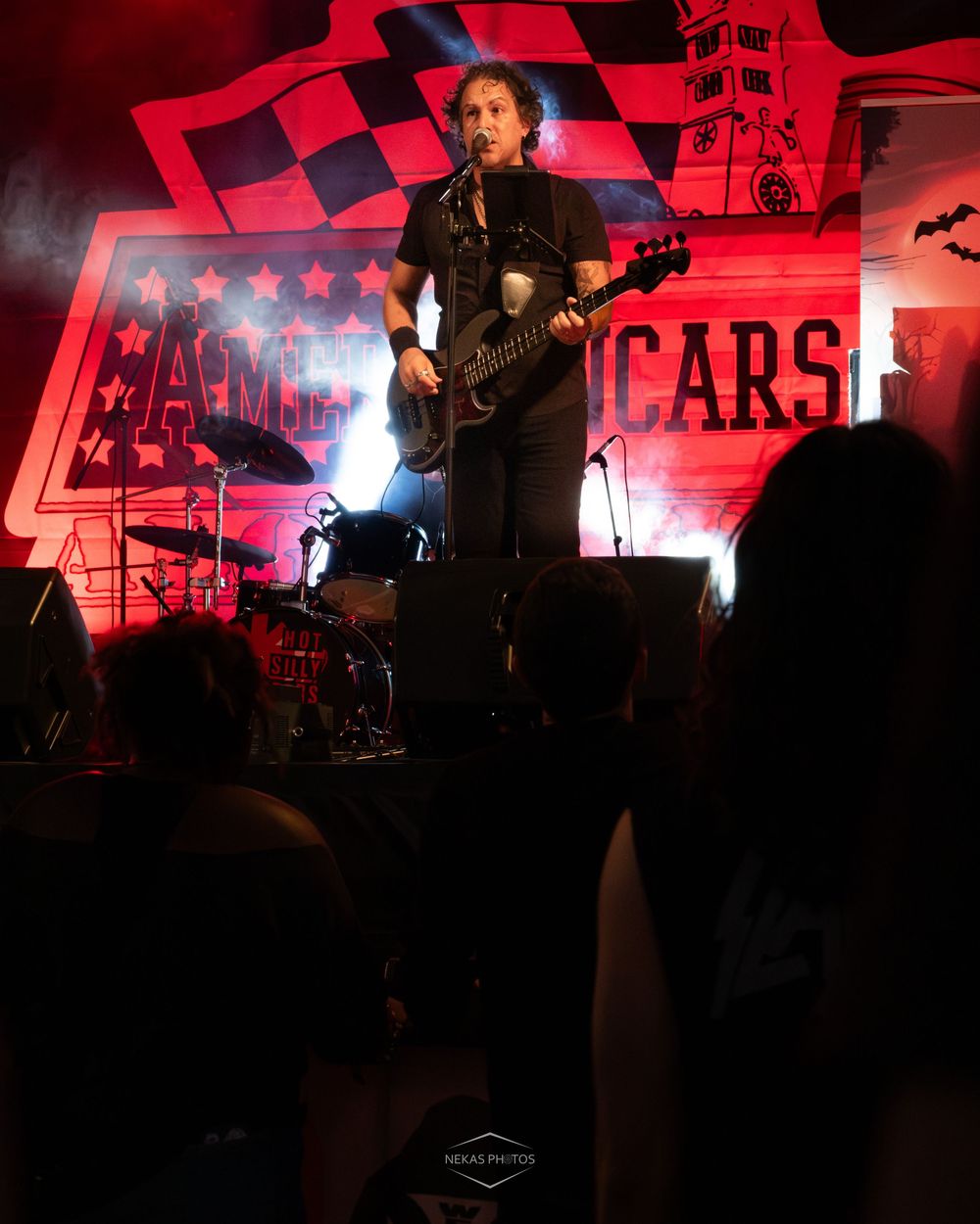 guitarist performing on stage at Americars event under red lights with crowd in foreground.