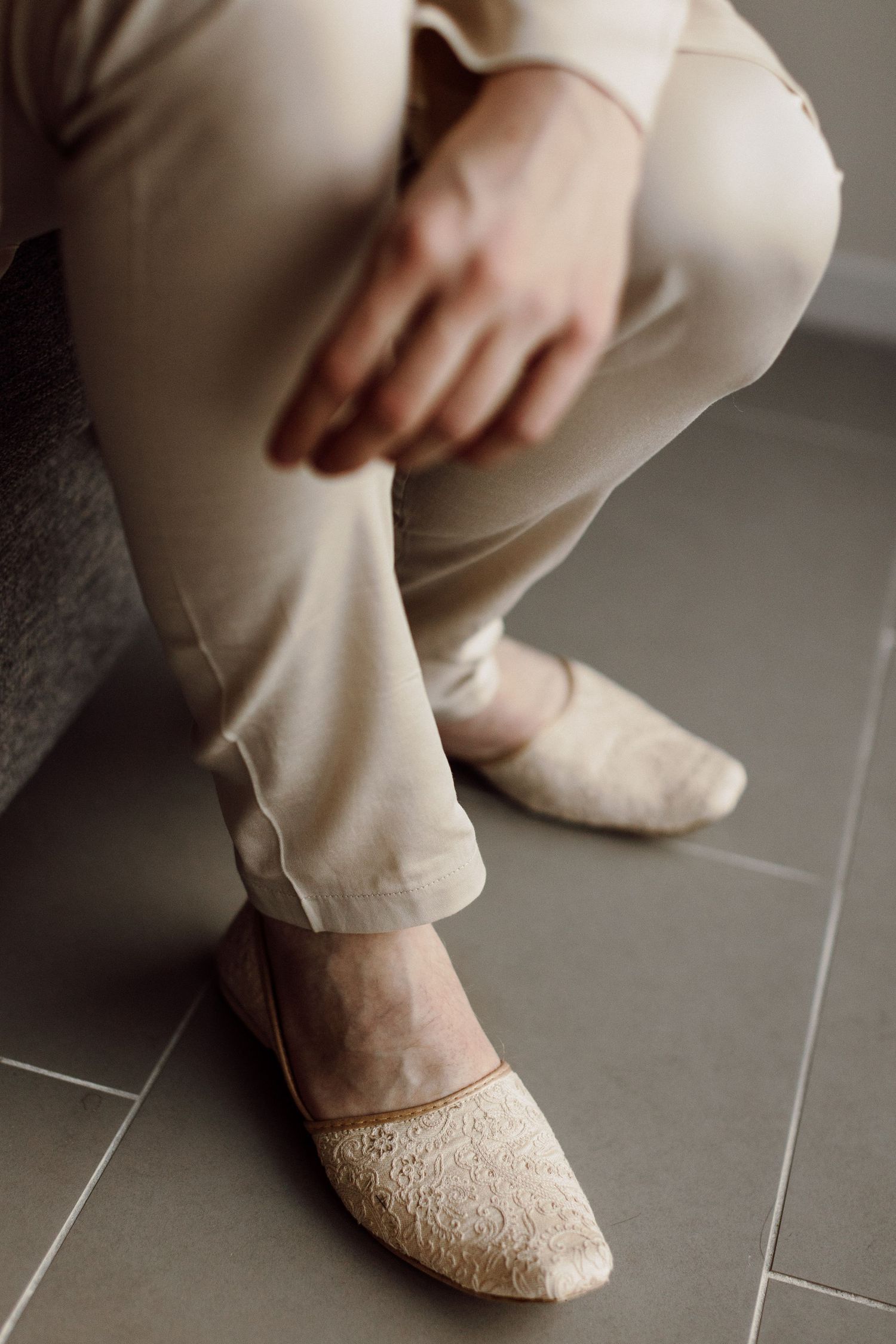 Groom wearing cream linen suit and decorative lace wedding shoes sits during Indian fusion wedding ceremony.