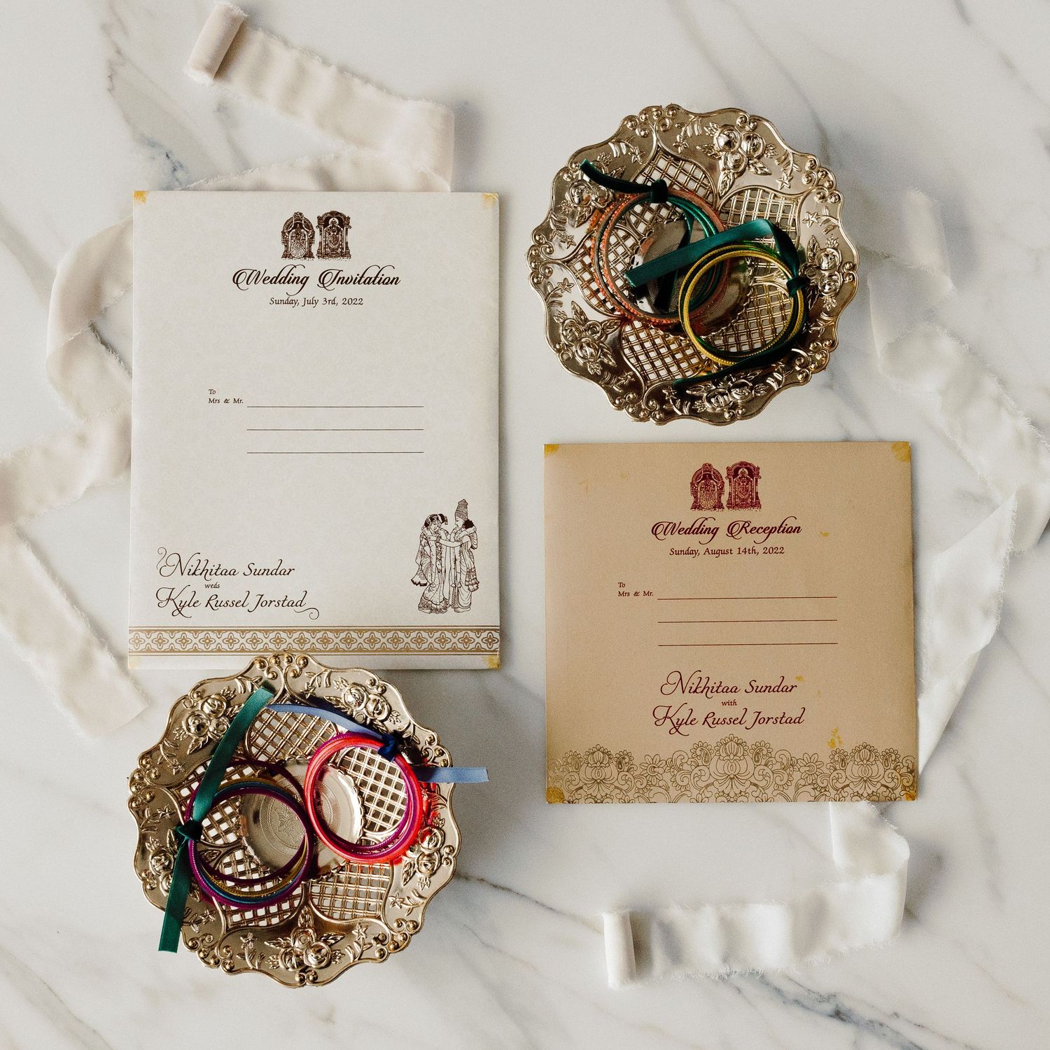 Indian wedding invitation suite with bangles and rings displayed on ornate gold trays.