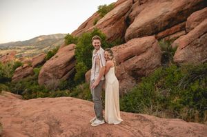 Couple in wedding attire posing on red rocks at Red Rocks Park Colorado during golden hour sunset.