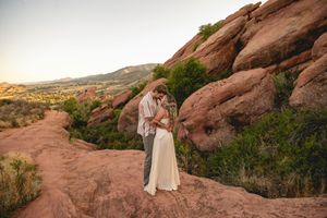 Couple embracing among red rock formations at Red Rocks Park, Colorado, at golden hour in wedding attire.