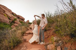 Bride and groom dancing on a red dirt trail surrounded by red rock formations and desert shrubs.