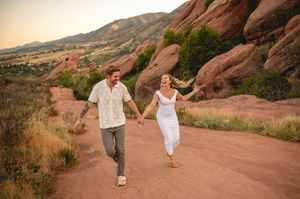 Couple holding hands running on a red rock trail at Red Rocks Park Colorado during golden hour sunset.