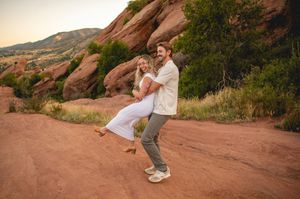 Couple dancing joyfully at Red Rocks Park, Colorado, surrounded by red rock formations and lush greenery at sunset.