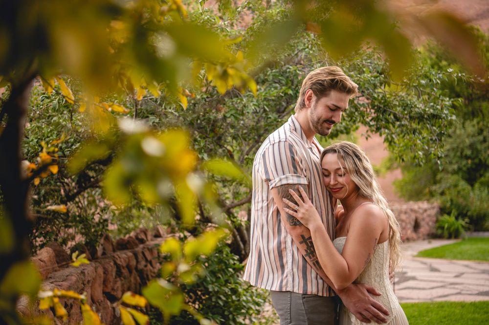 Couple sharing a romantic moment in a lush garden surrounded by colorful autumn foliage and red stone walls.