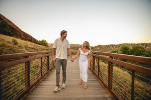 Couple holding hands walking on wooden bridge at sunset in scenic outdoor landscape.