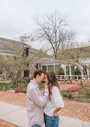 Romantic couple touching foreheads tenderly in a brick courtyard garden with blooming spring flowers.