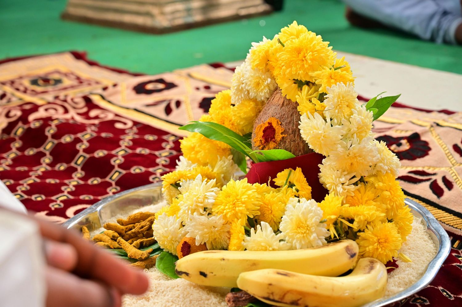 Woman in red salwar kameez arranging marigold flowers and diyas in rangoli pattern for Diwali celebration.
