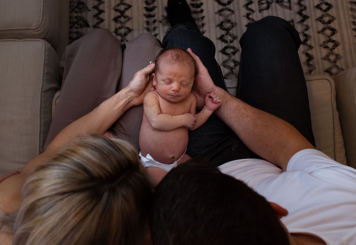 Adult hands gently supporting small baby lying on lap.
